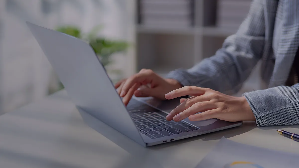 Das Foto zeigt die Hände über der Tastatur eines aufgeklappten Laptops. Der Rest der Figur ist im Bild nicht zu sehen, nur die Hände, die Arme und ein Stück des Oberkörpers; Sie können jedoch einen hellen Raum erkennen, wahrscheinlich ein Büro, und die Jacke, die die Figur trägt. Aus dem Kontext geht hervor, dass die Person an einem Laptop sitzt und arbeitet. Das Foto ist eine Cover-Grafik für die Success Story von Transition Technologies PSC und erscheint als Illustration für einen Beitrag mit dem Titel: Projektverwaltung in einer Kreativagentur. Jira Software + Add-ons.
