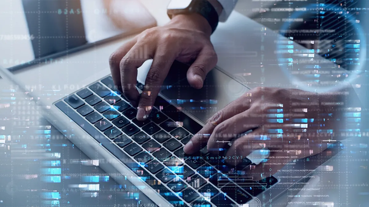 Zbliżenie dłoni osoby piszącej na klawiaturze laptopa. Na obraz nałożono grafikę cyfrową sugerującą zaawansowaną technologię lub cyberbezpieczeństwo, w tym diagram kołowy i linie kodu lub danych. Skupienie się na dłoniach i nakładka high-tech przekazują temat nowoczesnej, cyfrowej pracy lub komunikacji. Obraz notatki prasowej na temat: TransitionTechnologies PSC współpracuje z Oerlikon Surface Solutions w zakresie transformacji cyfrowej