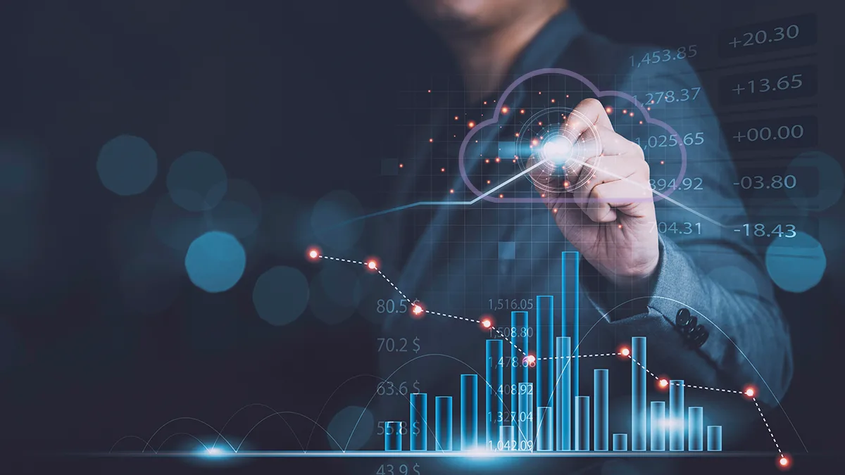 Na zdjęciu widzimy osobę w biznesowym stroju, która korzysta z futurystycznego interfejsu holograficznego. Interfejs wyświetla różne wykresy finansowe i punkty danych, sugerując analizę wyników biznesowych lub trendów rynkowych. To wizualne przedstawienie zaawansowanych możliwości analitycznych i innowacji technologicznych związanych z usługami chmurowymi Amazon Web Services. Obraz symbolizuje korzyści z modernizacji aplikacji w chmurze, pomagając firmom pokonać dług technologiczny i osiągnąć przewagę konkurencyjną.