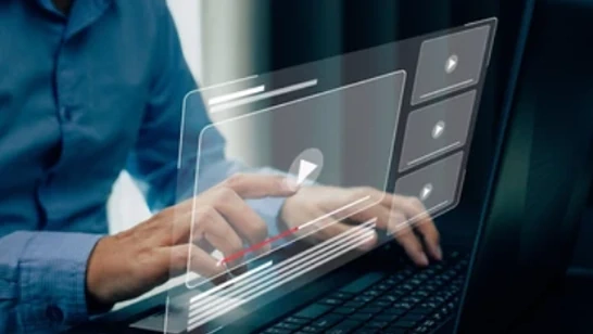 Eine Person, die einen Laptop mit einer futuristischen digitalen Schnittstellenüberlagerung verwendet, die interaktives Videolernen oder ein intelligentes Dashboard anzeigt. Die halbtransparenten Grafiken deuten auf Datenvisualisierung, Online-Tutorials oder eine digitale Betriebsplattform hin, die das Benutzererlebnis verbessert.