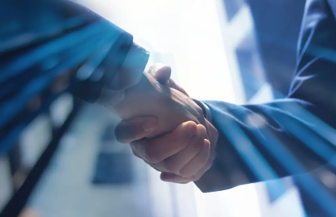 Two people in business attire shaking hands with sunlight streaming through.