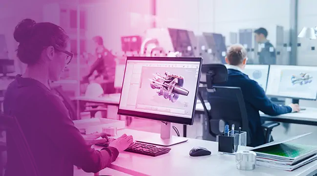 Engineers working on 3D mechanical designs using CAD software in an office setting.