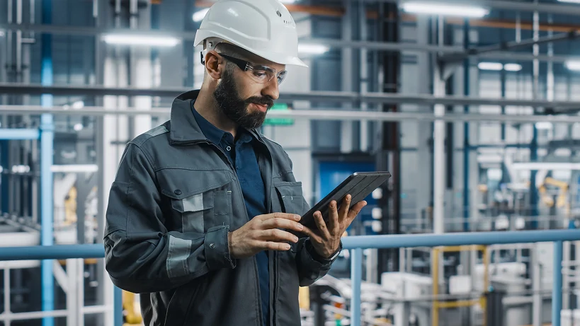 Engineer wearing a safety helmet using a tablet in a modern manufacturing facility.