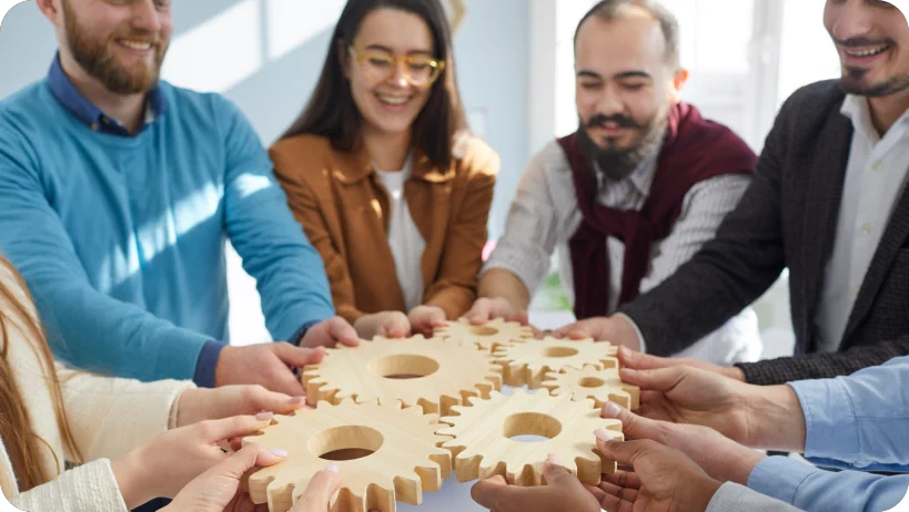 Zespół trzymający drewniane koła zębate symbolizujące współpracę i integrację.