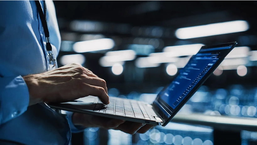 Specjalista IT korzystający z laptopa w nowoczesnej serwerowni, symbolizujący oparte na chmurze zarządzanie cyklem życia produktu (PLM) i cyfrową transformację.