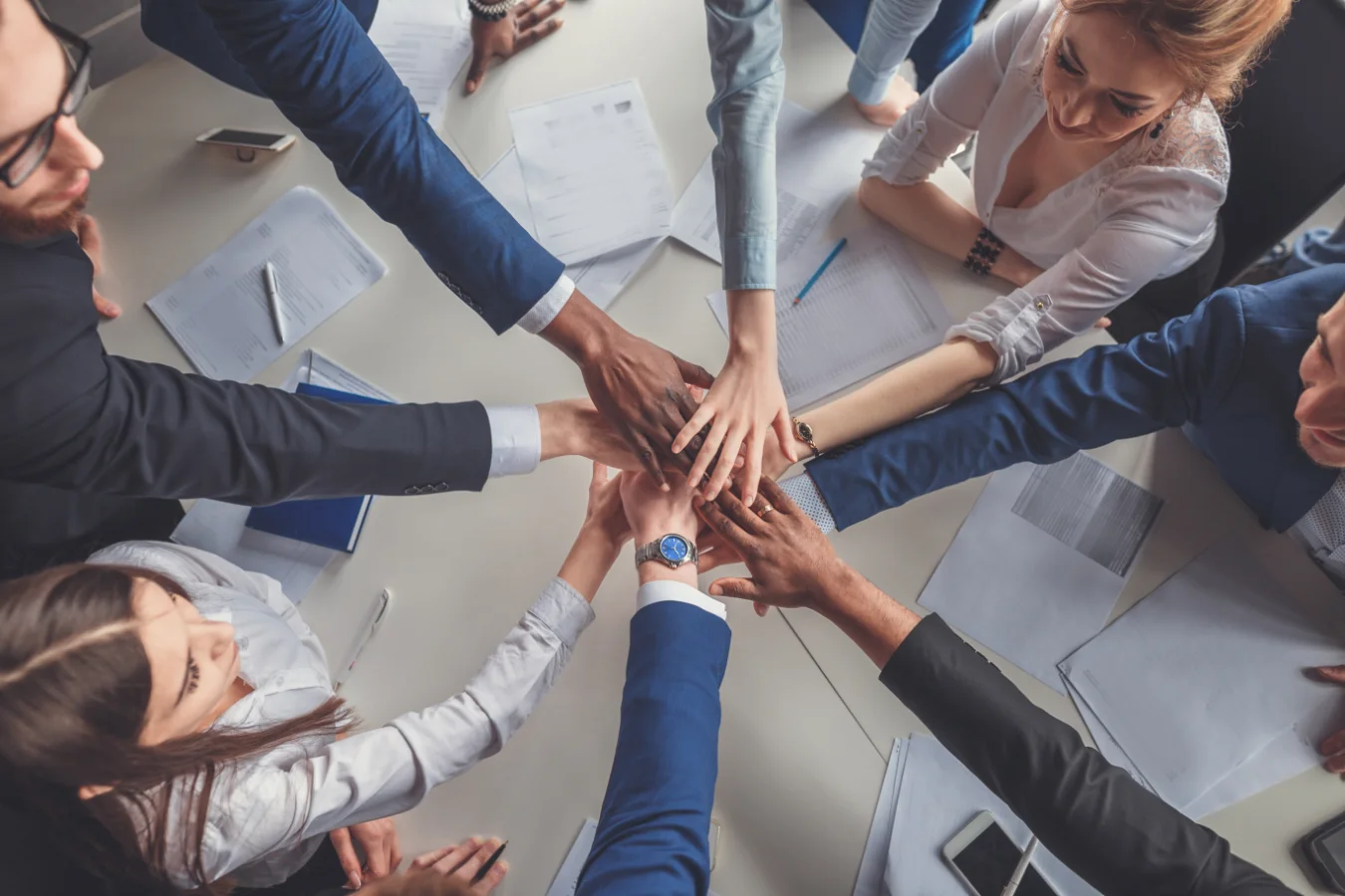 Large group of people holding hands over a table.