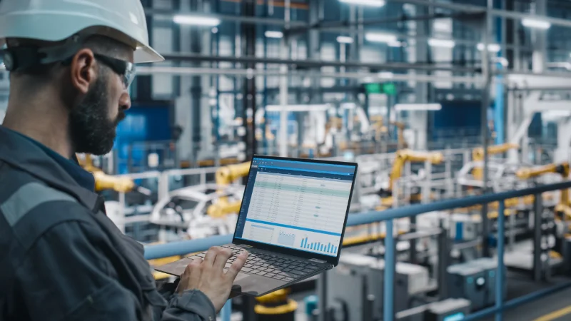 Ingénieur utilisant un ordinateur portable avec des tableaux de bord de données dans une usine intelligente – représentant l'IoT industriel et la surveillance de la production en temps réel.