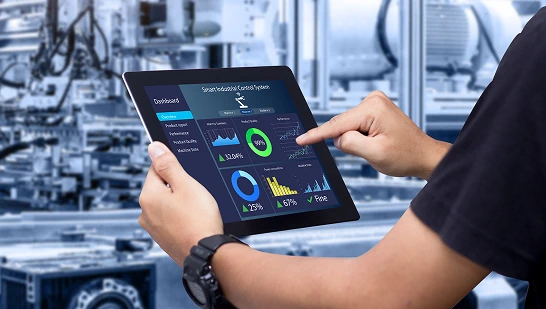 Person interacting with a digital dashboard on a tablet in an industrial automation or manufacturing environment, displaying performance metrics and graphs.