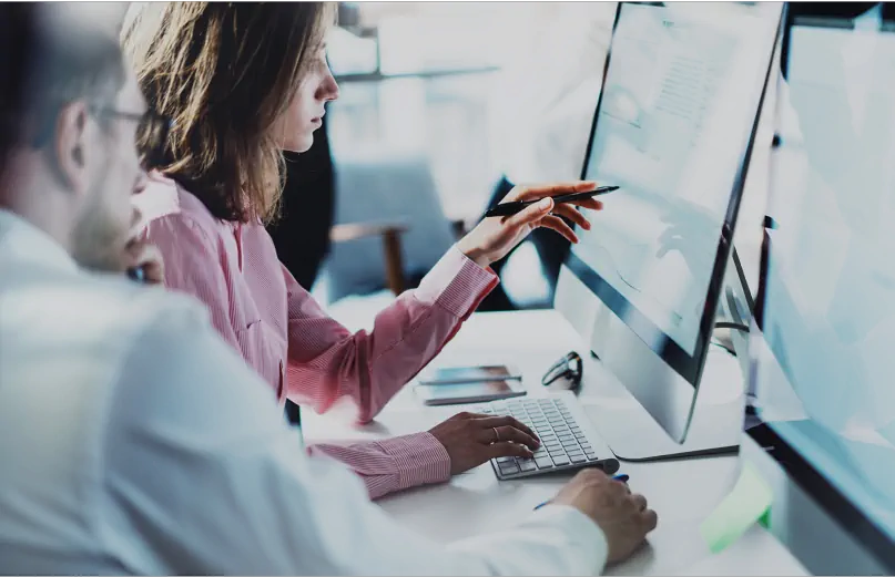 Dwóch współpracowników pracuje razem przy komputerze, a jeden z nich wskazuje na ekran.