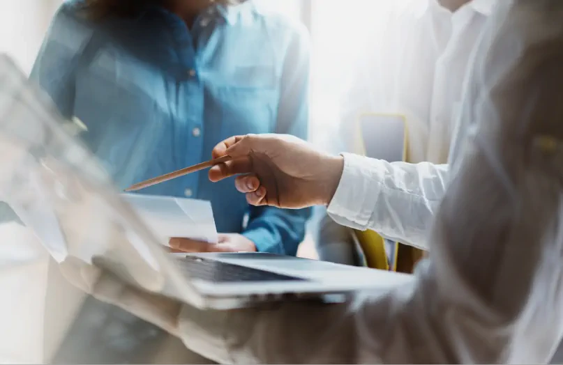 Dwie osoby współpracują przy laptopie, a jedna z nich wskazuje ekran ołówkiem.