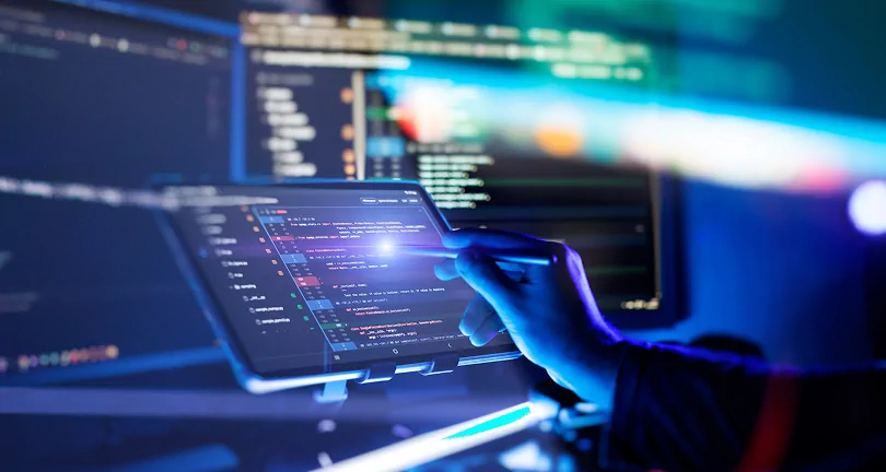 Developer using a stylus on a tablet with source code in a futuristic blue-lit workspace with multiple monitors