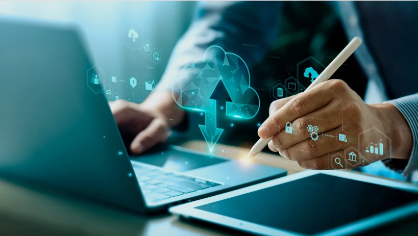 Ein Geschäftsmann verwendet einen Laptop und ein Tablet mit einer digitalen Cloud-Computing-Konzeptüberlagerung, die PLM (Product Lifecycle Management) in der Cloud symbolisiert.