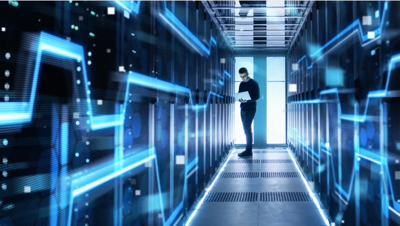 IT-Spezialist arbeitet an einem Laptop in einem futuristischen Rechenzentrum, umgeben von beleuchteten Server-Racks und digitalen Netzwerkgrafiken, die Cloud-basiertes PLM (Product Lifecycle Management) und digitale Innovation repräsentieren.